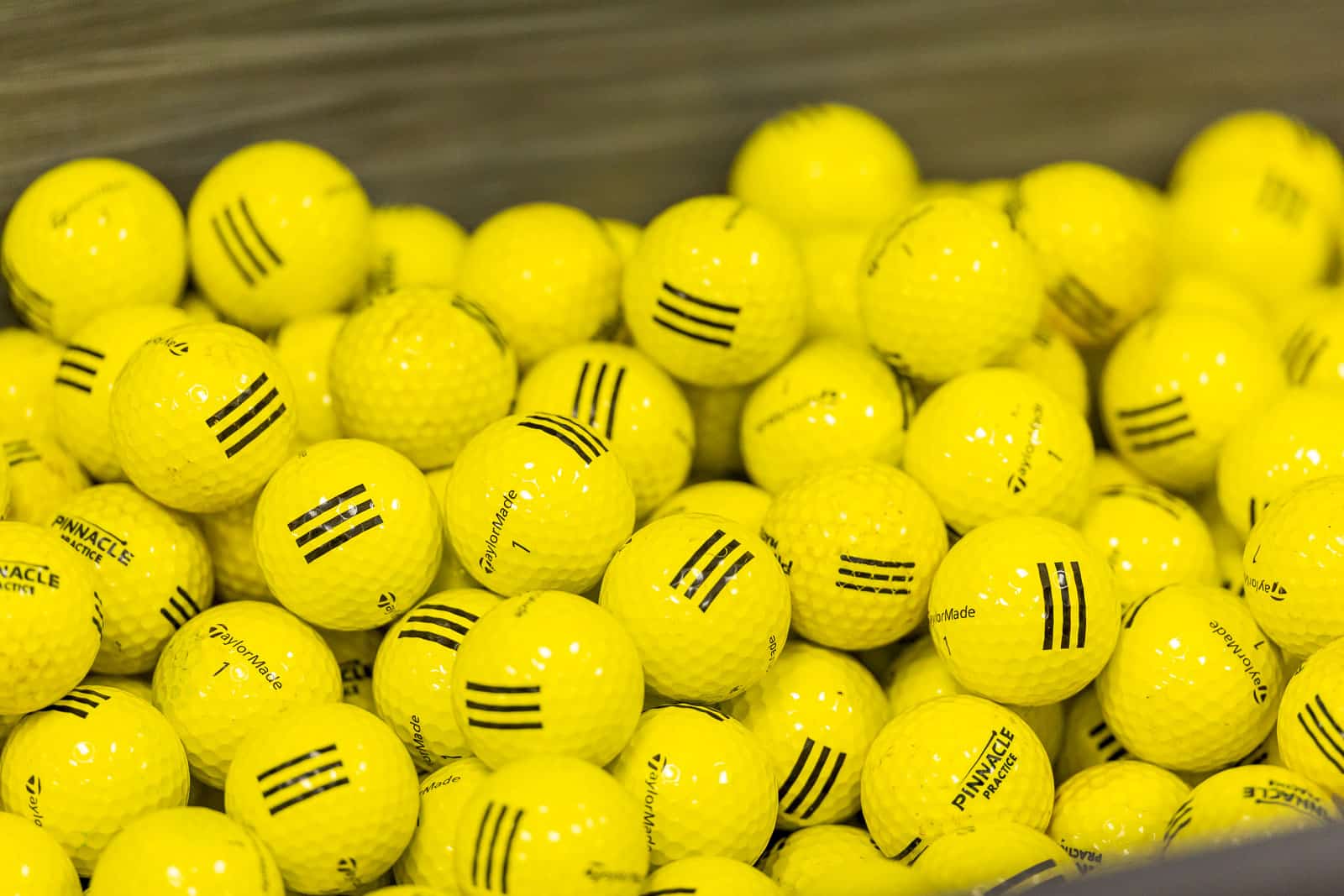 Pile of yellow golf balls with black markings and TaylorMade branding in a heap on a surface.