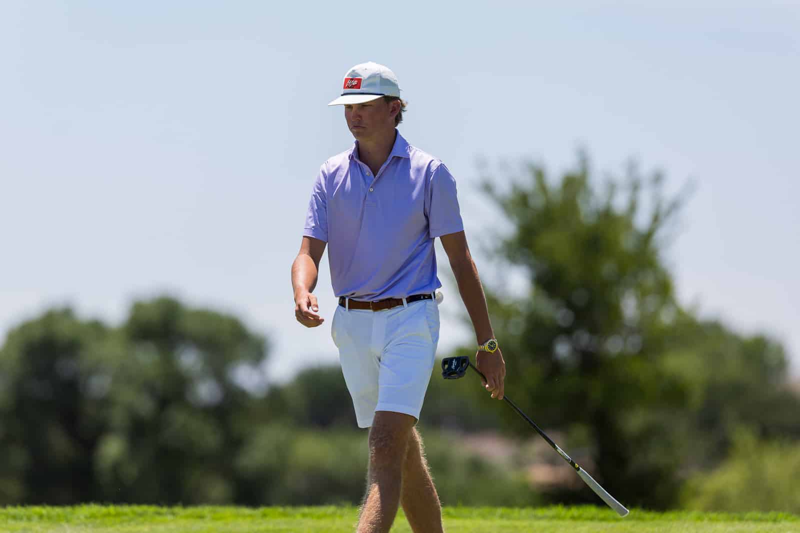Golf or mini-photoshoot: a man in a purple polo and white shorts walking on a golf course, holding a club and rangefinder, under sunny skies
