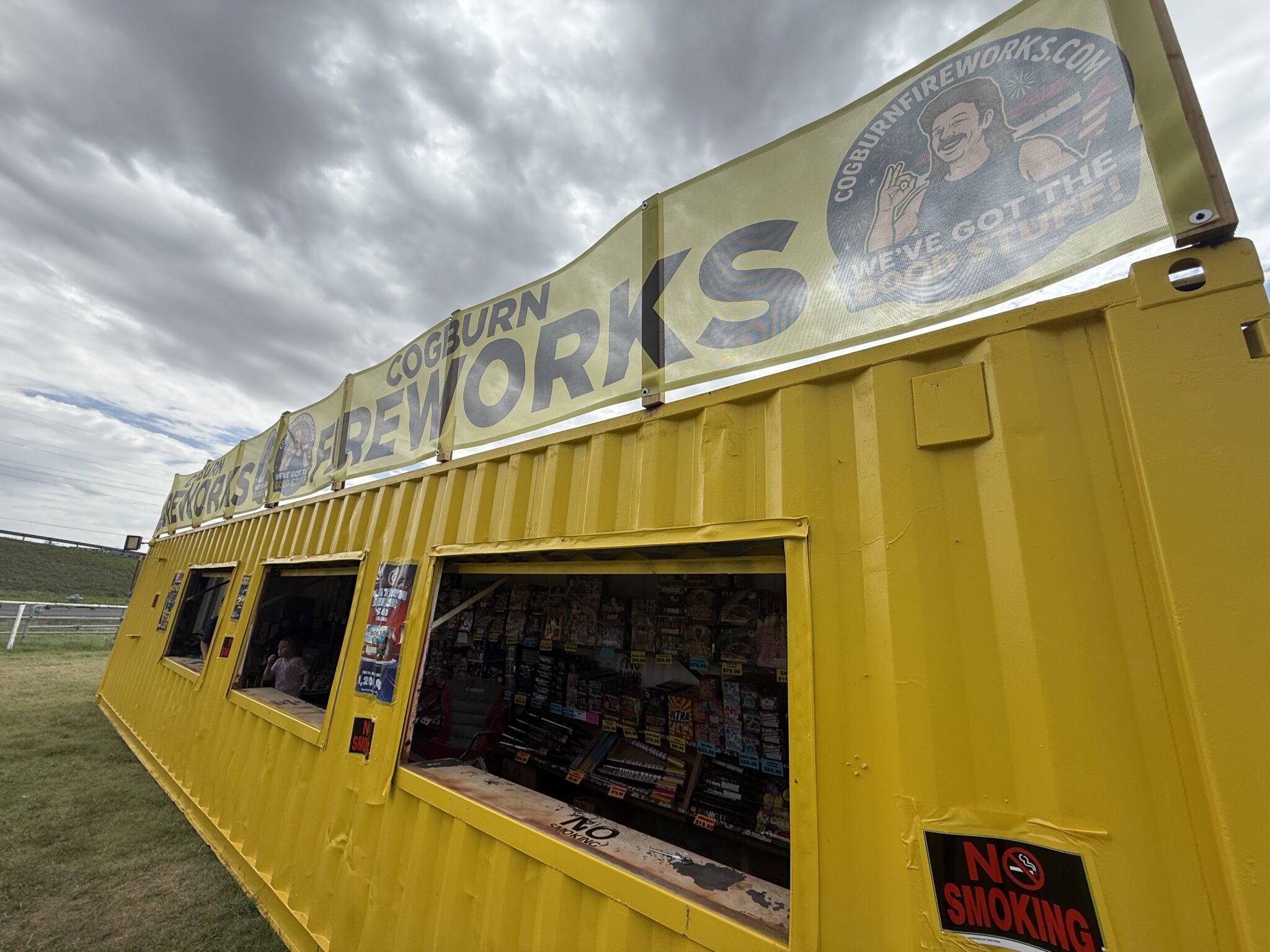 IMG_5645 | Press Pass Sports Bright yellow kiosk with open storefront windows selling magazines, against a cloudy sky.