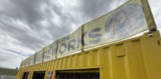 Bright yellow kiosk with open storefront windows selling magazines, against a cloudy sky.