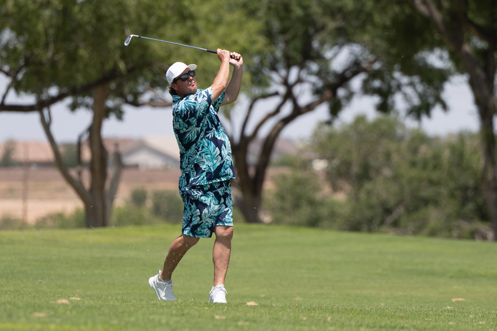 Golfer in tropical-style outfit mid-swing on a sunny golf course.