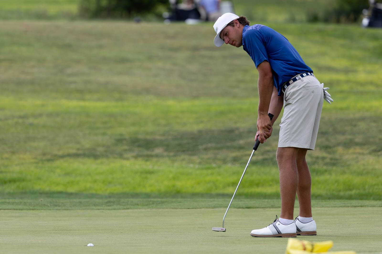 Male golfer in a blue shirt and white cap preparing a putt on the green.