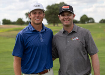 TheBud-68 | Press Pass Sports Two men stand side by side smiling on a golf course, wearing polo shirts and baseball caps with sponsor logos, greenField background.
