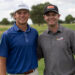 Two men stand side by side smiling on a golf course, wearing polo shirts and baseball caps with sponsor logos, greenField background.