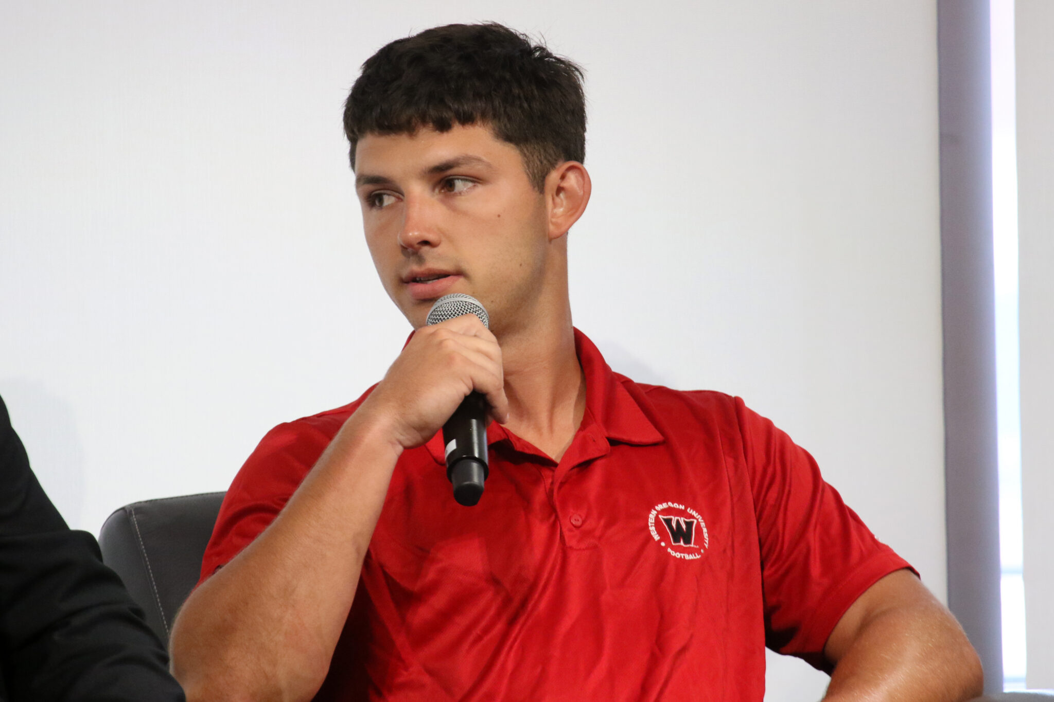 Jordan McCarty - Western Oregon | Press Pass Sports Man wearing a red polo shirt speaking into a handheld microphone