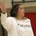 1K6A4889 | Press Pass Sports Woman in a white jacket raises her left hand in the air, facing to the right in a gym-like setting.