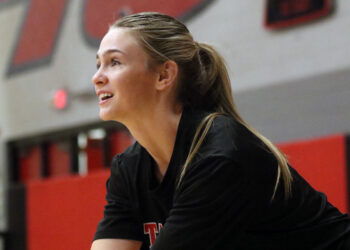 1K6A5057 | Press Pass Sports Woman in a gym, side profile with blonde ponytail, wearing a black top, captured in mid-action against a red and gray background.