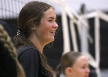 1K6A4234 | Press Pass Sports Side profile of a smiling young woman with long brown hair, indoors among a crowd.