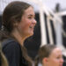 1K6A4234 | Press Pass Sports Side profile of a smiling young woman with long brown hair, indoors among a crowd.