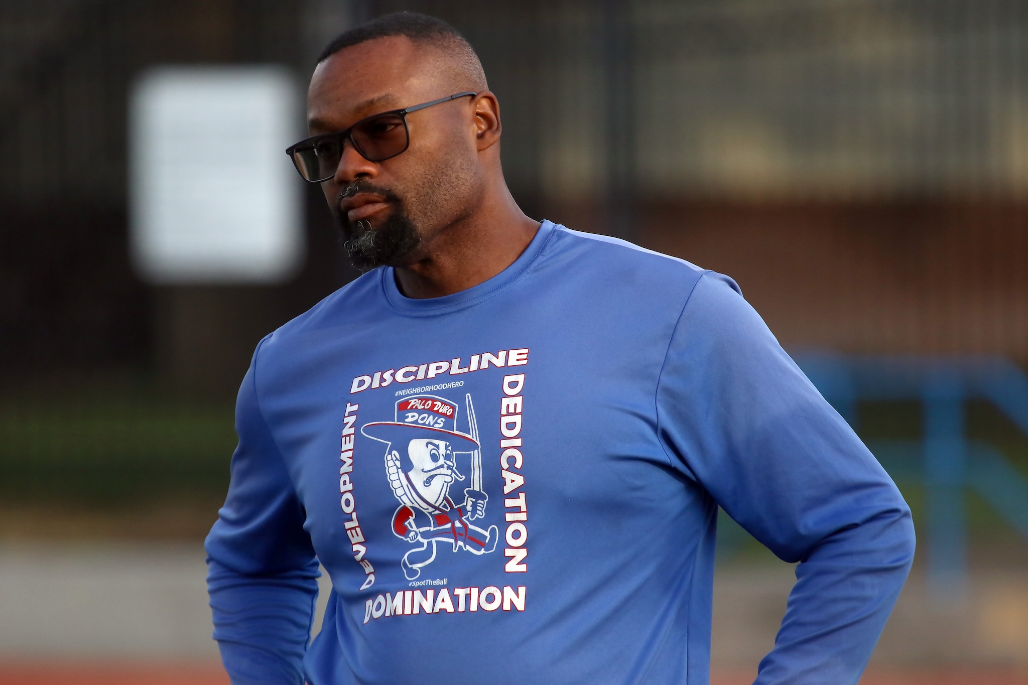 Man wearing a blue graphic T-shirt outdoors, with hands on hips and a focused expression.