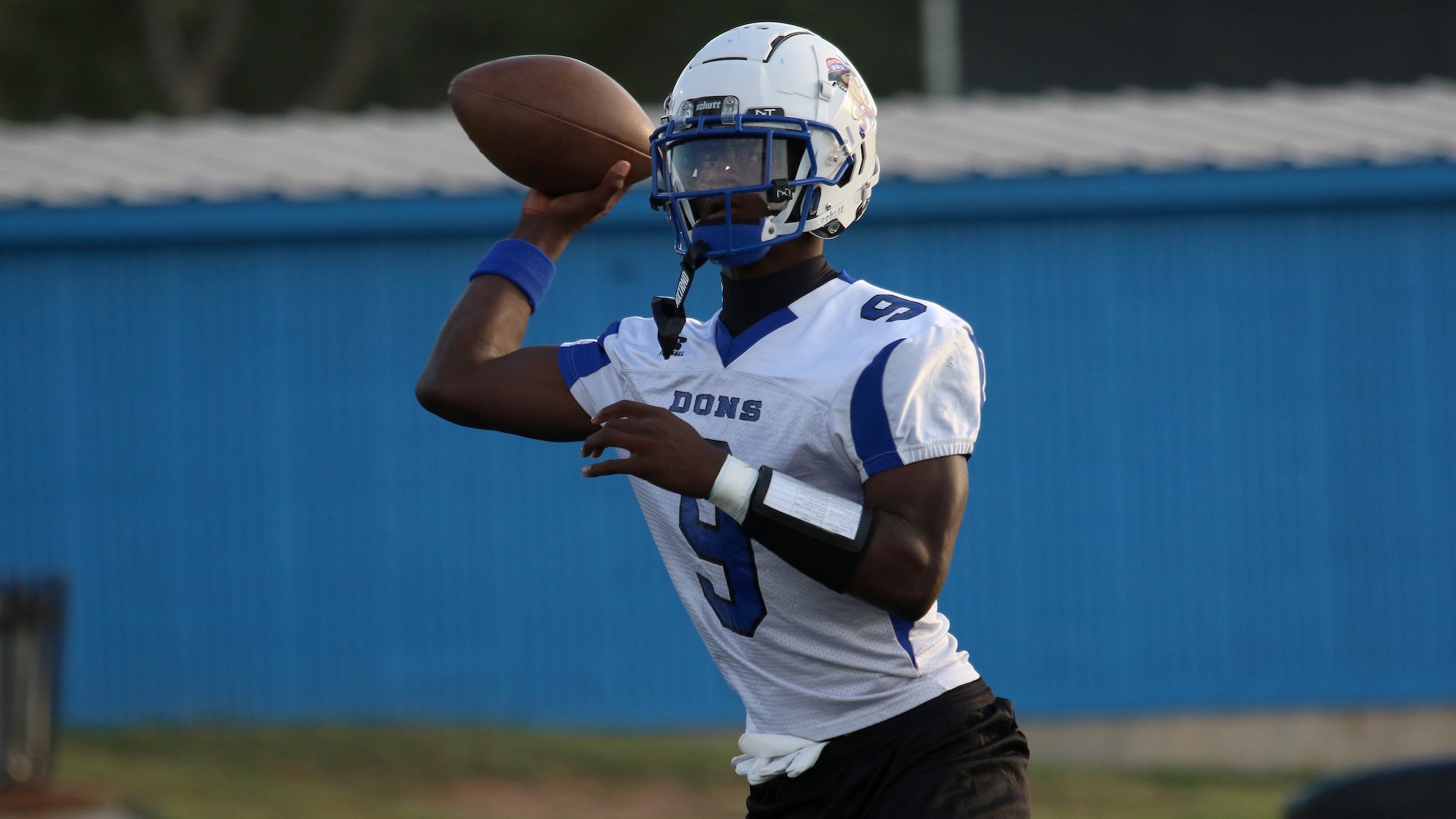 Football quarterback in a white and blue uniform mid-throw on a field
