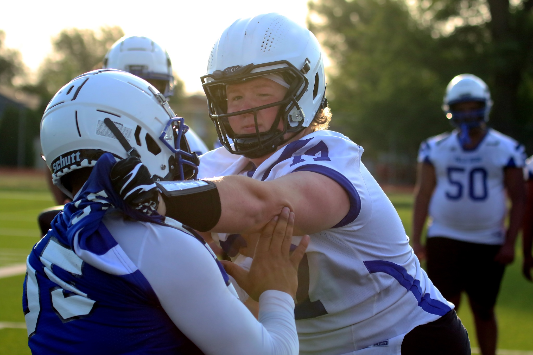 Two football players in white and blue uniforms hug on a sunny football field during a game.