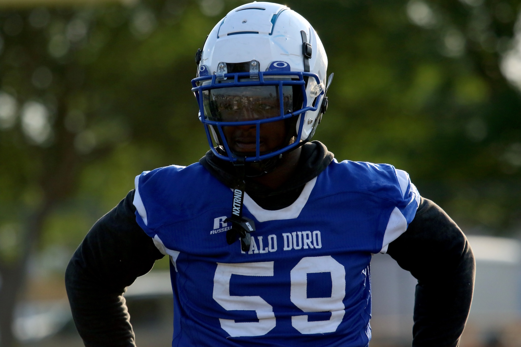 American football player in a blue jersey with the number 56 and a white helmet with a blue face mask outdoors.