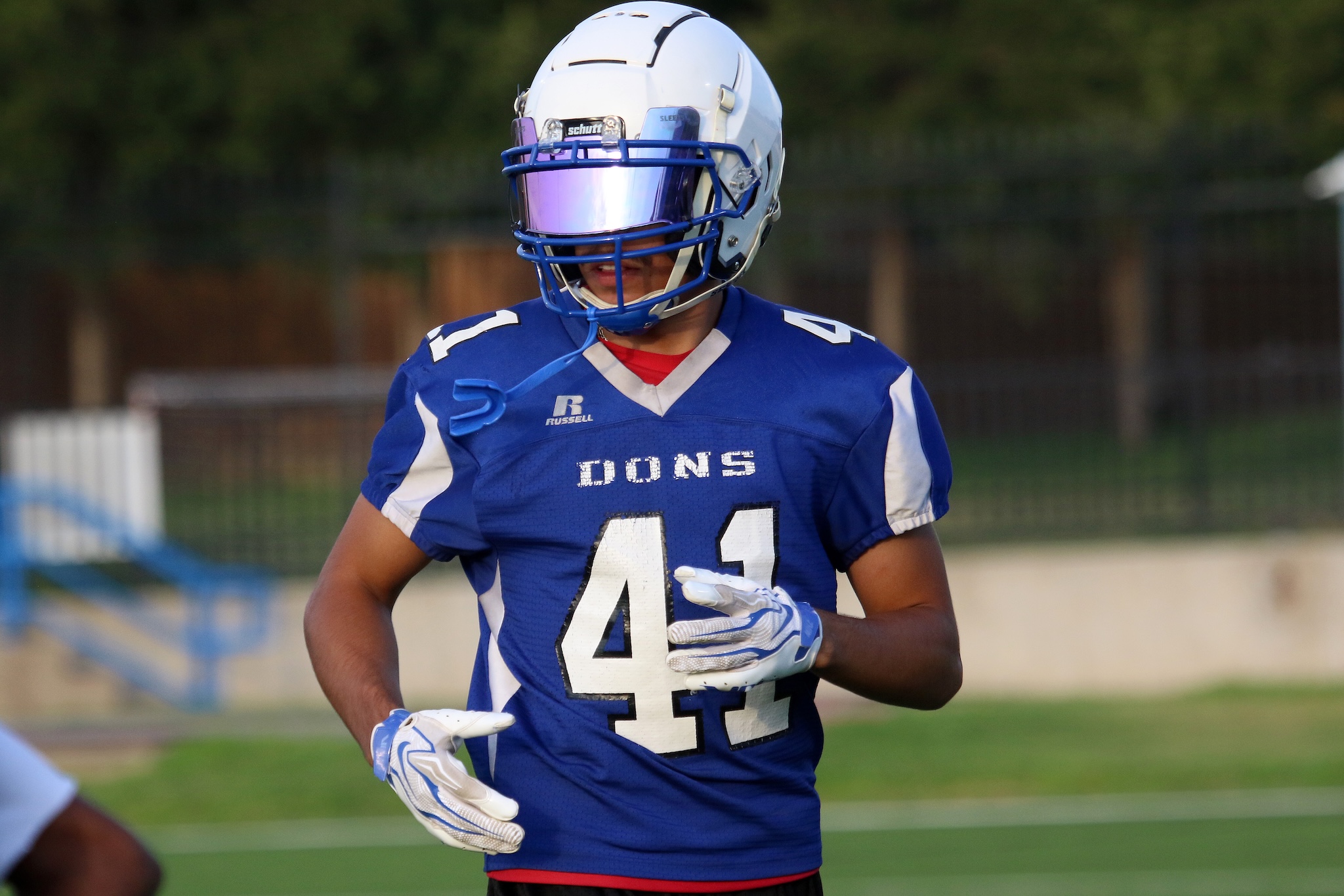 American football player wearing a white helmet and blue jersey with number 41, running on a field during a game.”,