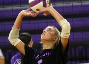 1K6A4422 | Press Pass Sports Female volleyball player with beige arm sleeves reaching up to touch a purple-and-white ball near the net.