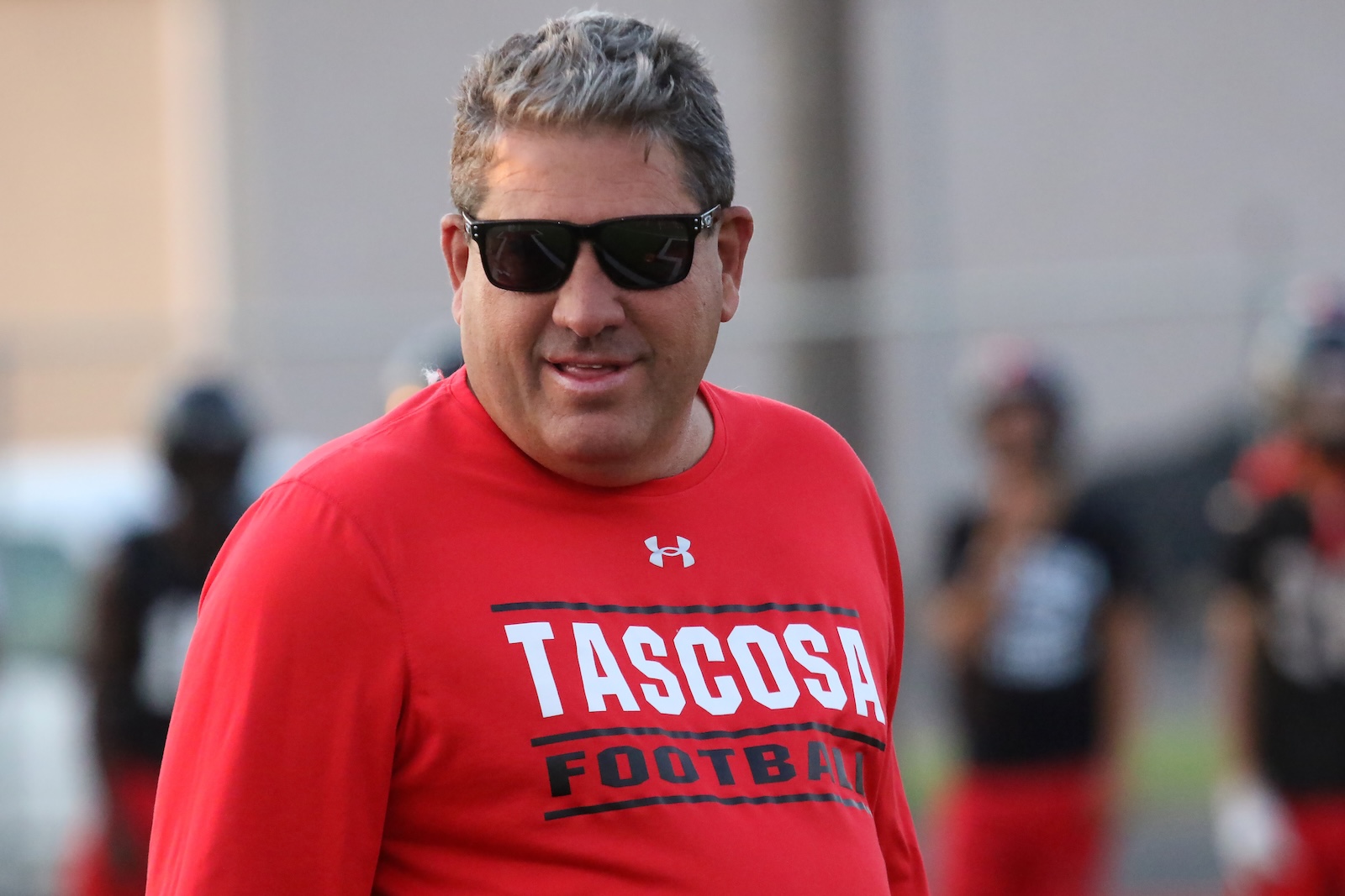 Man in red TASCOSA Football shirt and sunglasses outdoors, facing camera with a slight smile.