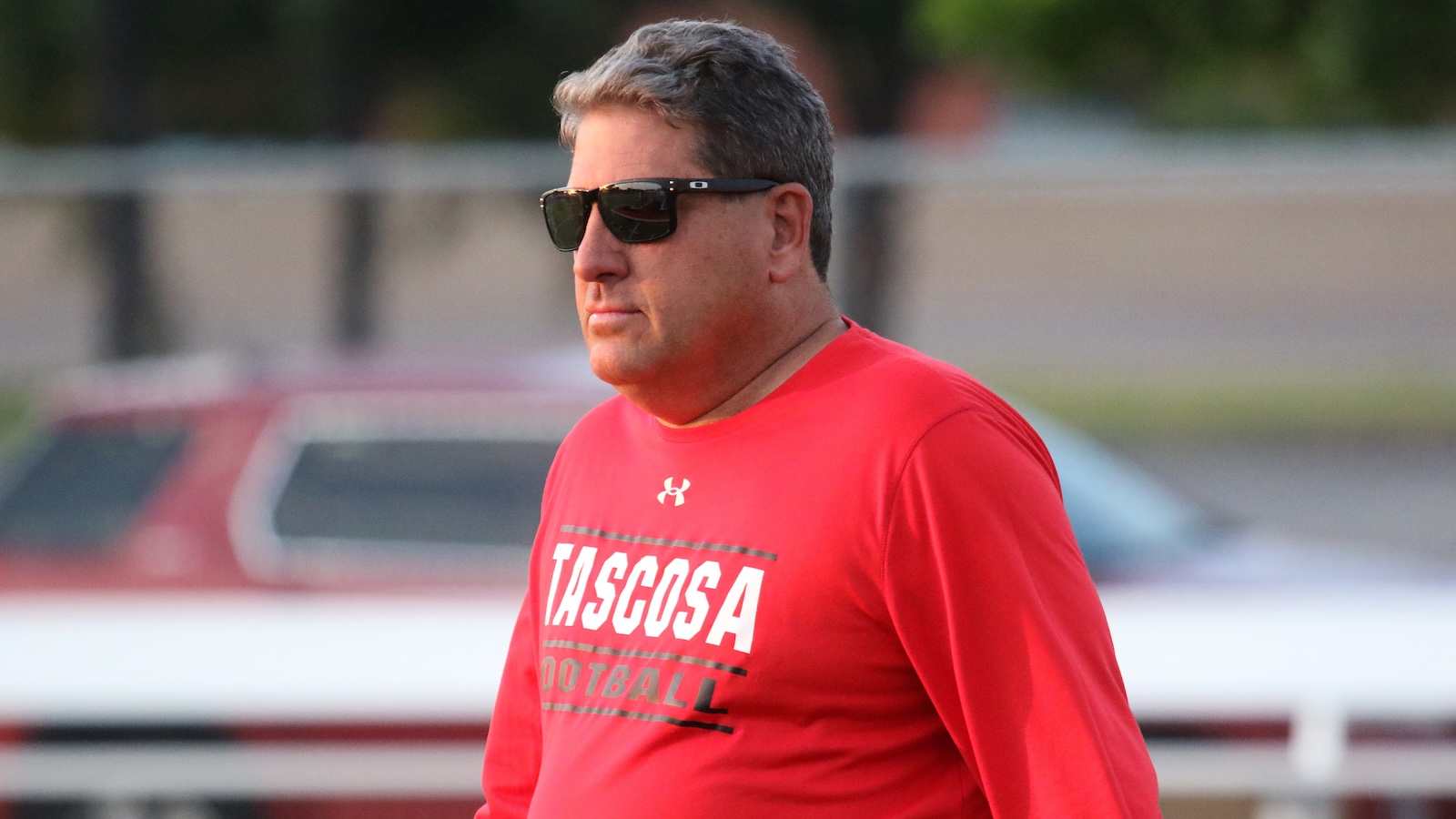 Side profile of a man in a red Tascosa Football shirt wearing dark sunglasses.