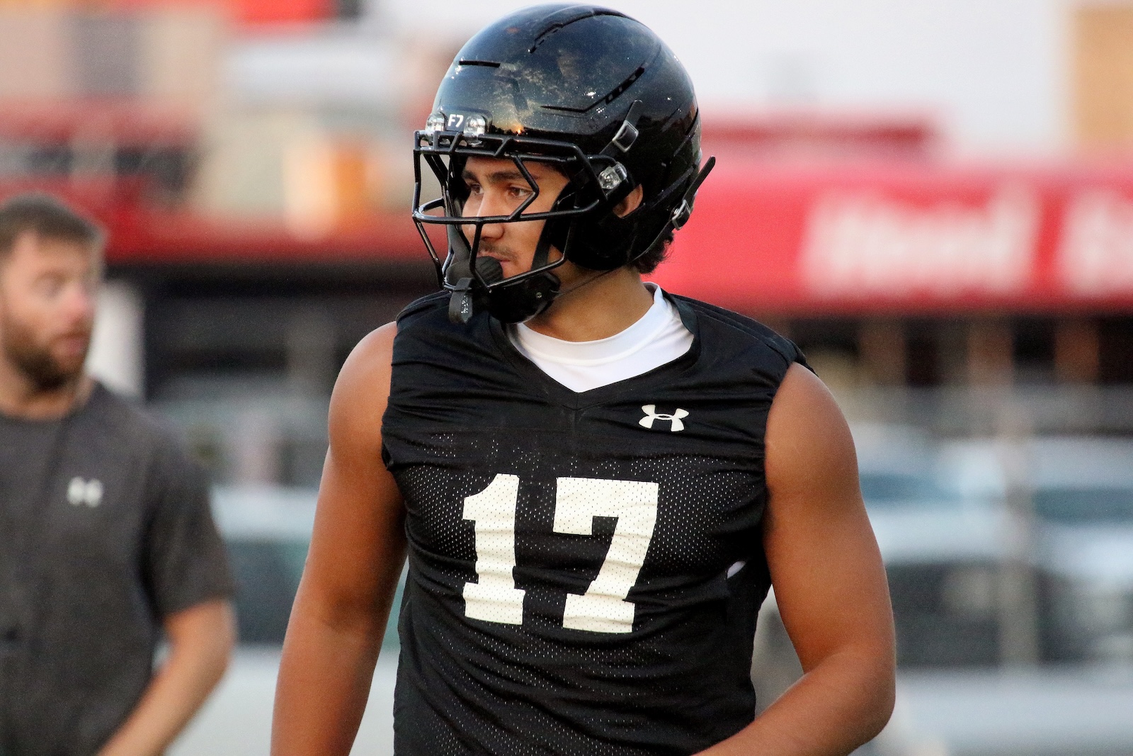 Football player in a black jersey and helmet with the number 17, looking to the left on a practice field.