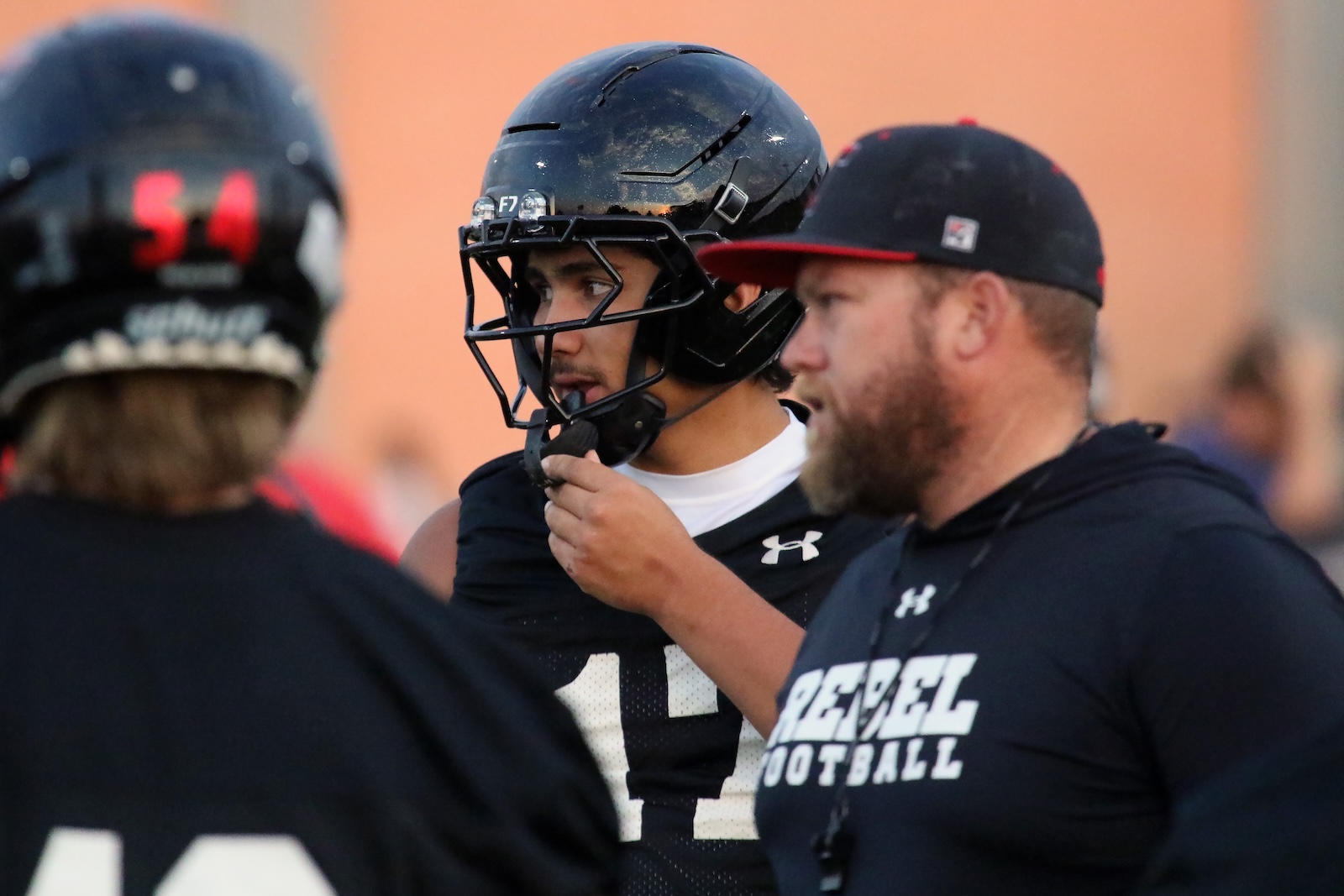 Football player in a black helmet and jersey listening to a coach during practice.