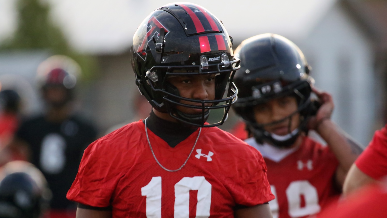 Football player in a red jersey #10 with a black helmet, focused during practice.
