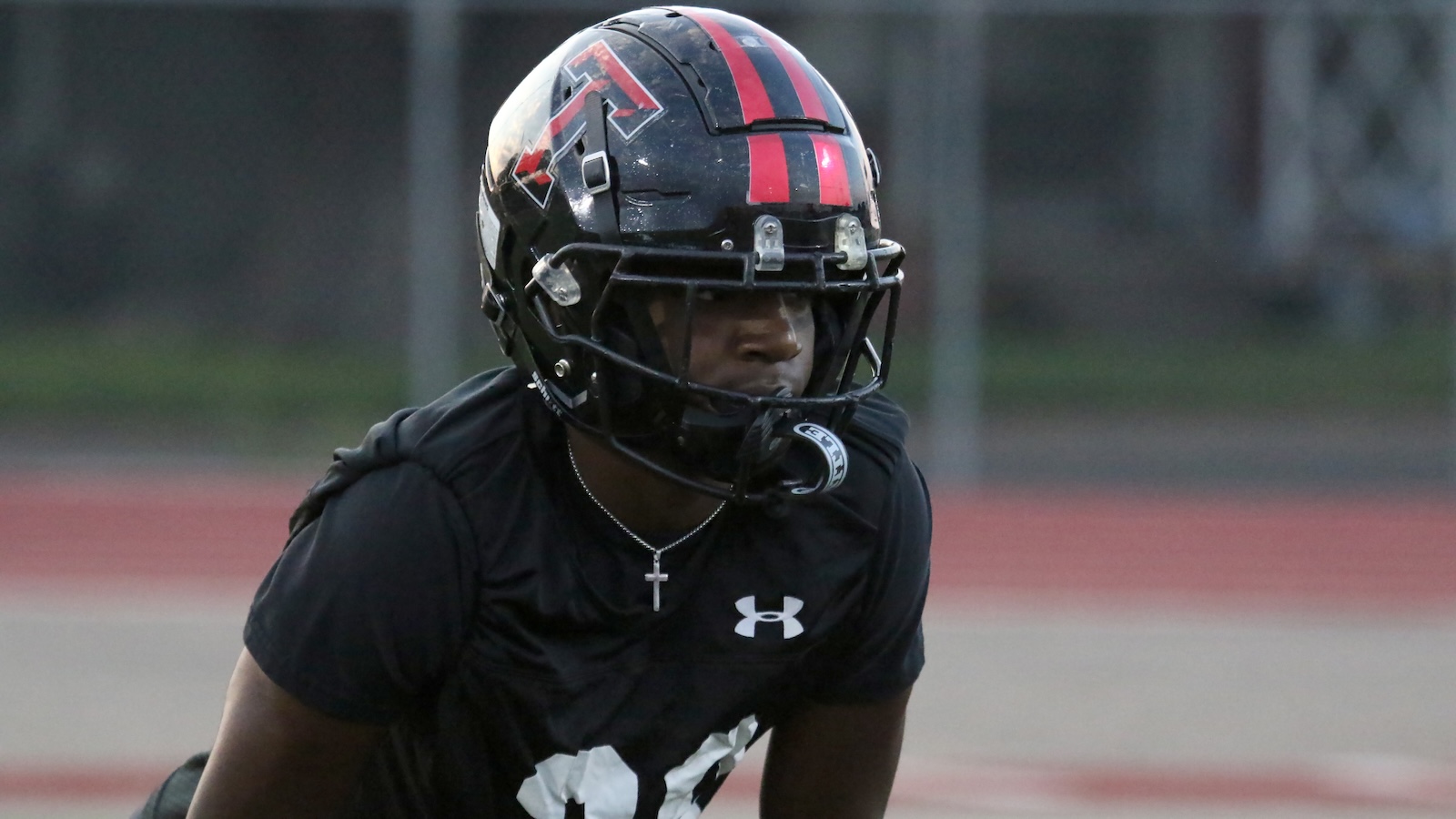 Football player in a black Under Armour jersey and helmet with red stripes on a track field.