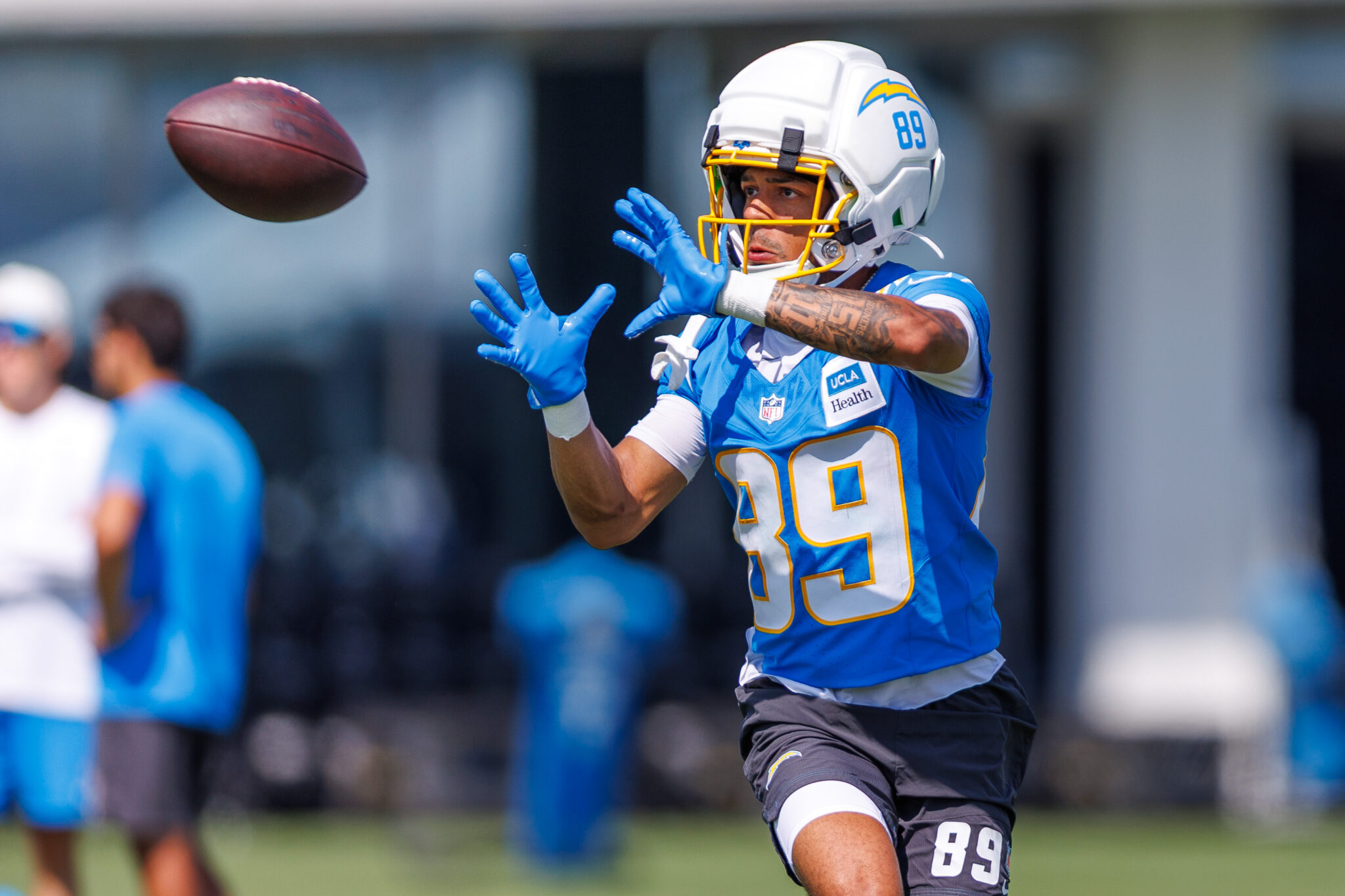 IMG_6289 | Press Pass Sports Football player in a blue jersey (#89) reaching to catch a spiraling ball, white helmet with yellow facemask in action.