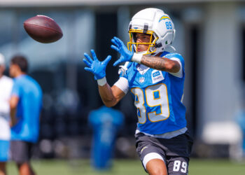 Football player in a blue jersey (#89) reaching to catch a spiraling ball, white helmet with yellow facemask in action.