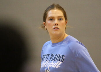 1K6A5628 | Press Pass Sports Woman with light brown hair tied back, wearing a blue athletic shirt with 'West Plains' text, looking off to her right in a gym or indoor setting.