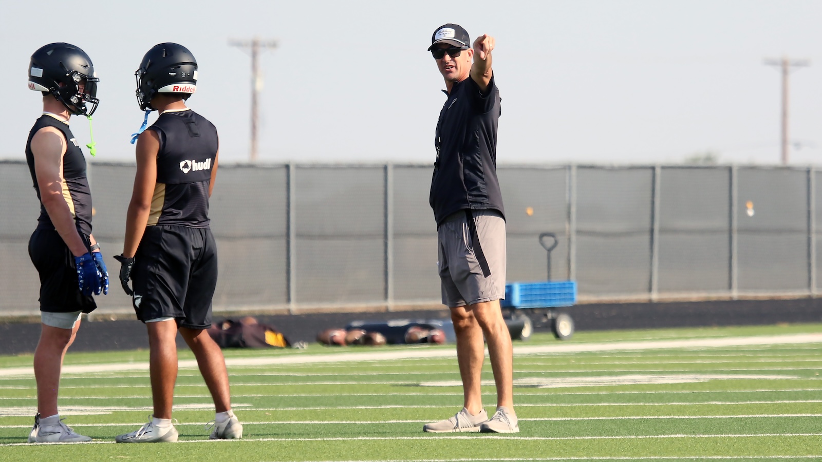 Football coach gives instructions to two players during practice on an artificial turf field.