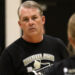 1K6A6166 | Press Pass Sports Middle-aged man with gray hair in a black Bushland volleyball t-shirt, looking to the left in a gym setting.