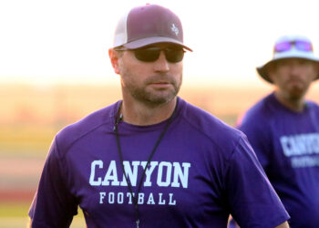 1K6A8625 | Press Pass Sports Man in purple Canyon Football shirt with cap and sunglasses, on a field with another player blurred in background at sunset.