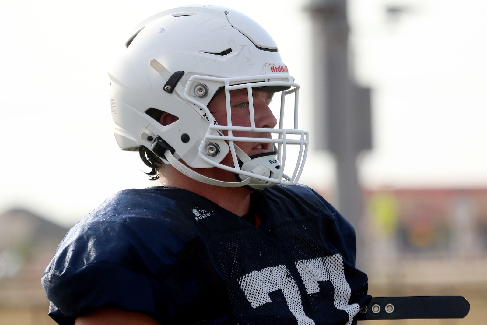 Football player wearing a white helmet with faceguard, looking to the right on the field.