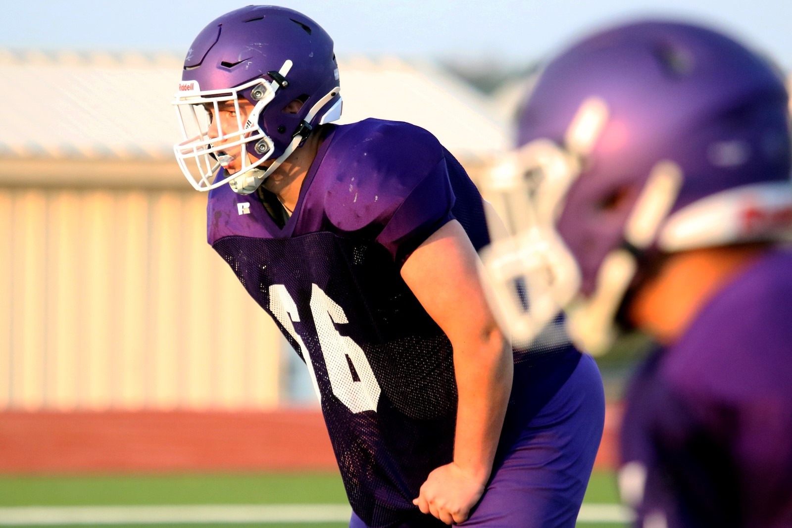 Football player in a purple jersey and helmet crouches in a ready stance on the field, preparing for the play.
