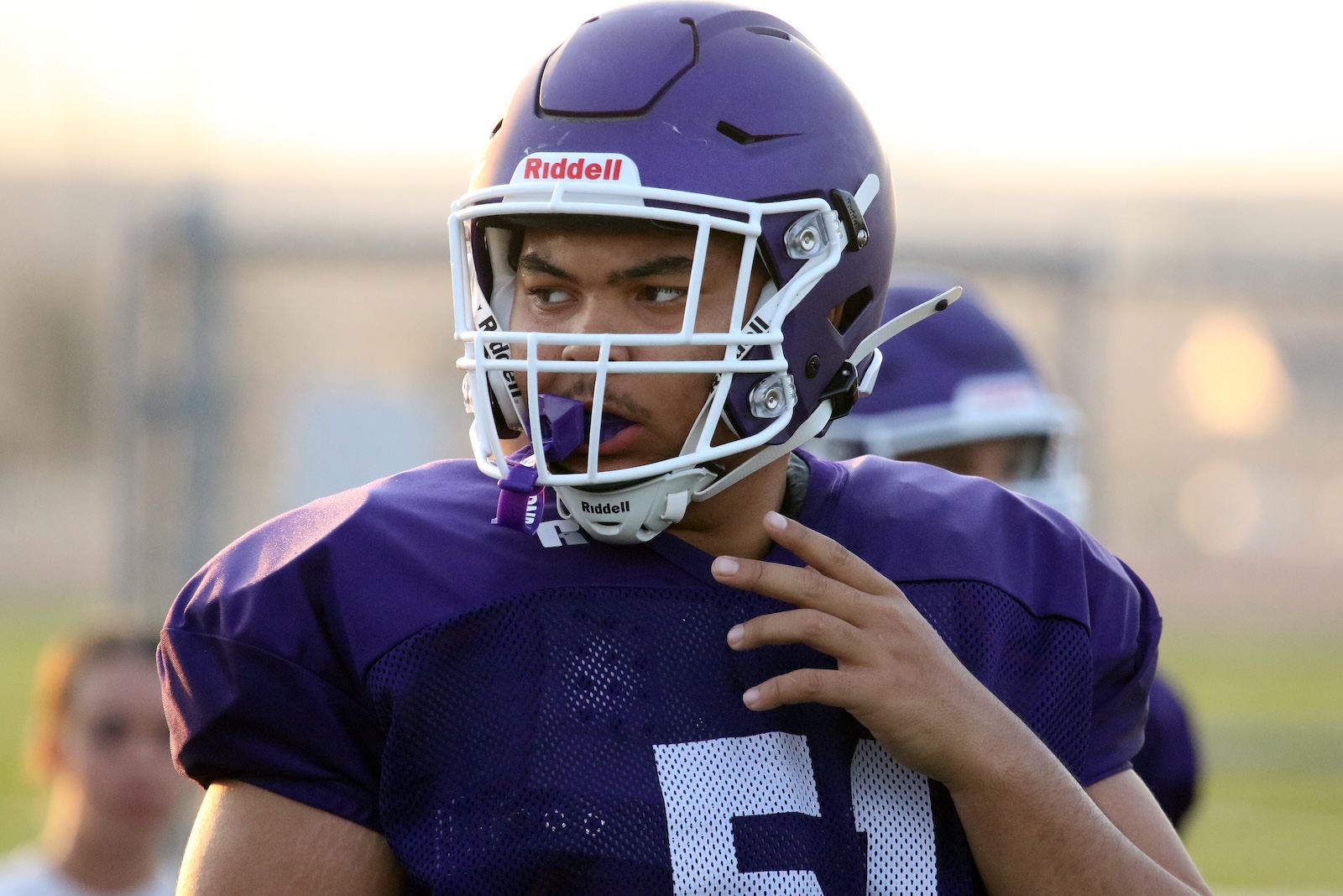 Football player in a purple uniform with a white facemask, looking to the left during practice.