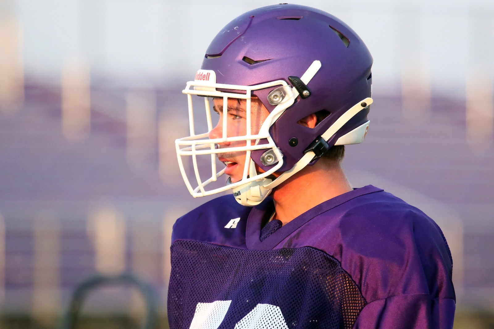 Side-profile of a football player wearing a purple helmet and jersey, focused during practice on a sunny day.
