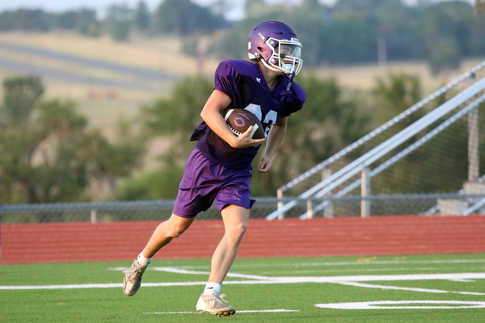 Young football player in a purple uniform runs with the ball on a grassy field during a game.
