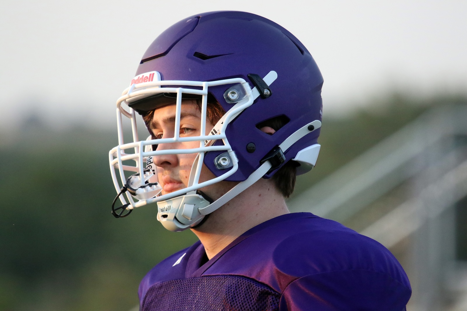 Close-up of a football player wearing a purple helmet with a white facemask, gazing to the left.