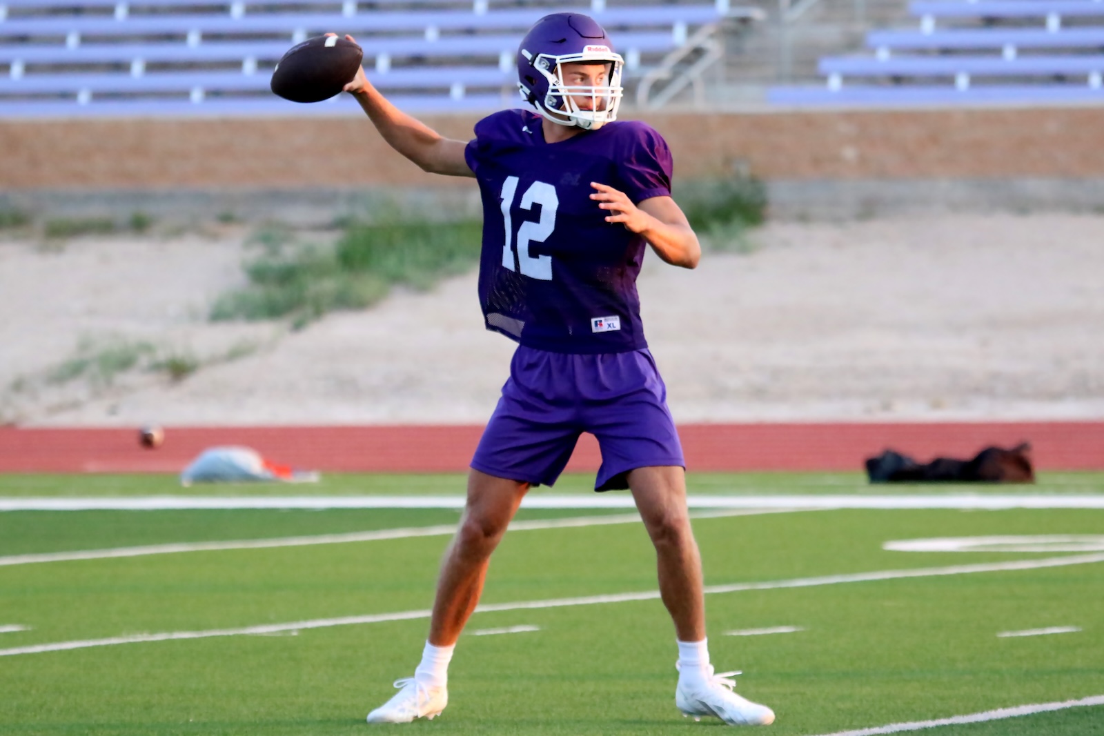 Quarterback in purple uniform (number 12) mid-throw on a practice field.