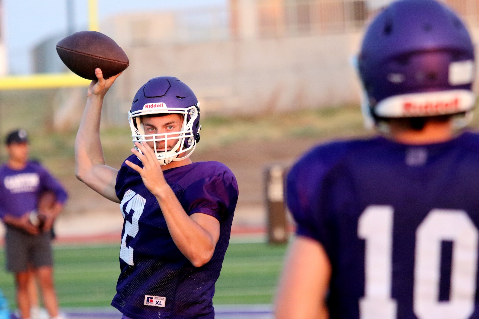 Quarterback in a purple jersey throws a football during a game, helmet on, focused gaze toward the target.