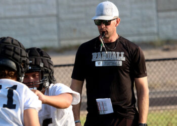 Randall - Dan Sherwood 2 | Press Pass Sports Coach wearing a white cap and sunglasses blowing a whistle while guiding football players on a field