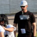 Randall - Dan Sherwood 2 | Press Pass Sports Coach wearing a white cap and sunglasses blowing a whistle while guiding football players on a field