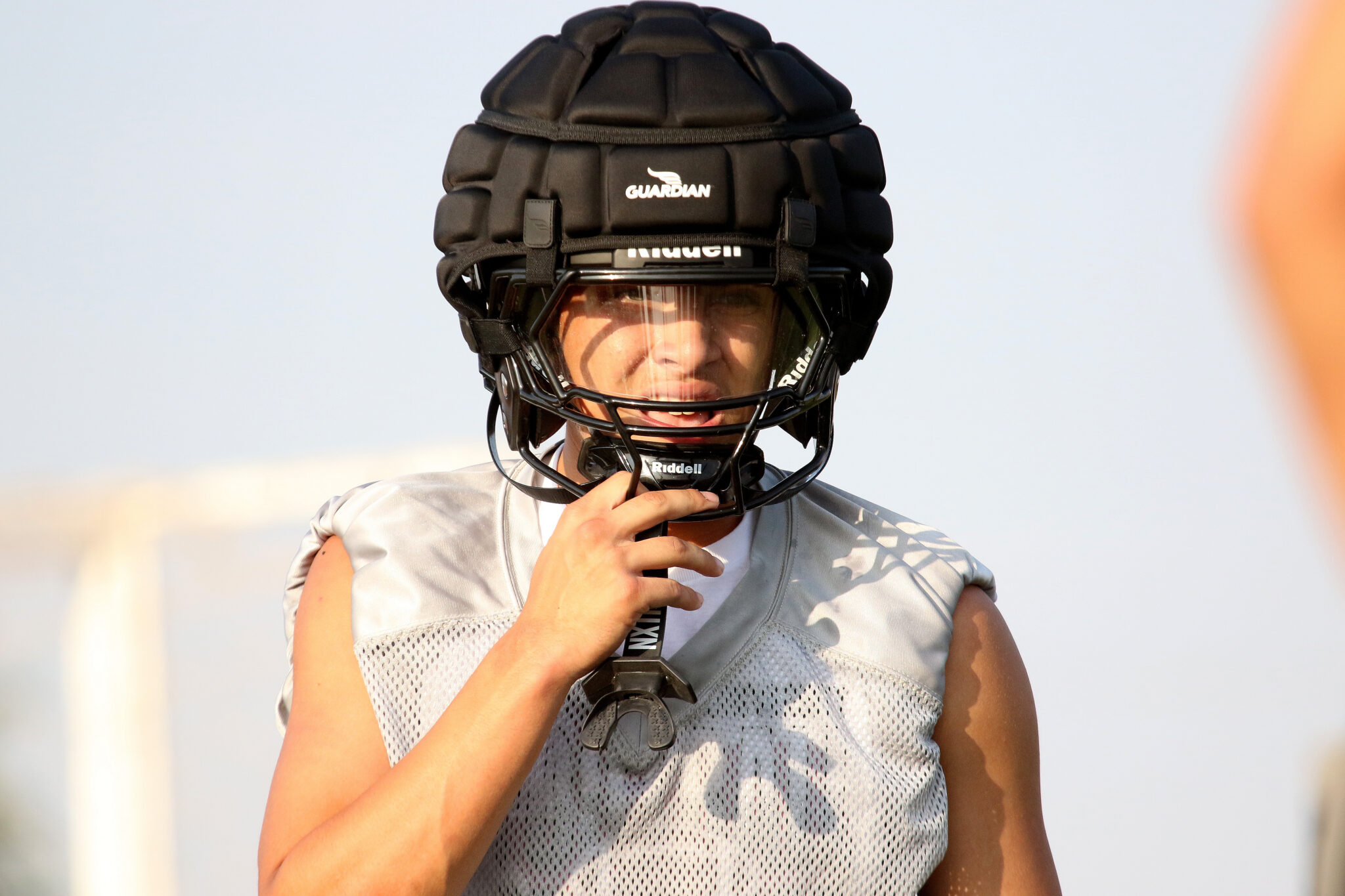 Randall - Drayden Ray 2 | Press Pass Sports Person wearing a black football helmet with faceguard, adjusting the chin strap outdoors. (informative)