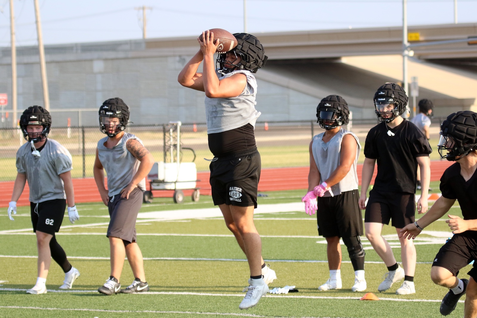 Player in mid-air catches a football during practice as teammates watch on the field.
