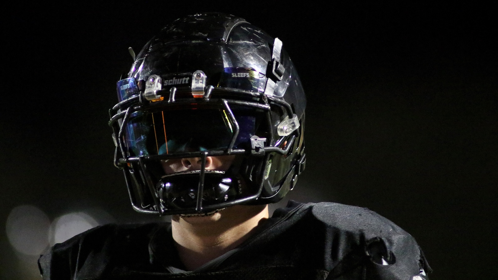 Close-up of a football player wearing a black Schutt helmet with a faceguard at night.