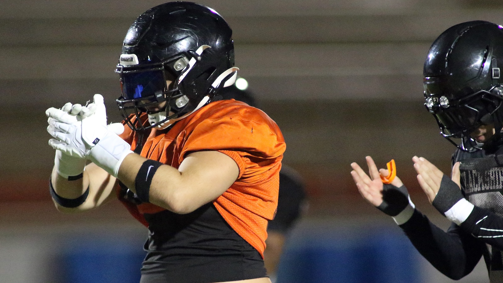 Football player in an orange jersey claps hands during a play, wearing a black helmet and white gloves.