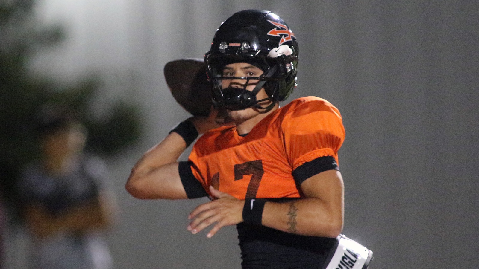 Quarterback in orange jersey number 7, black helmet, throwing a pass during a football game.
