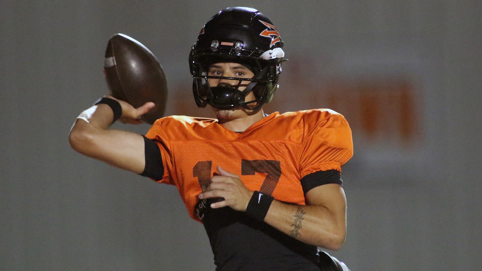 Quarterback in orange jersey (number 17) winds up to throw a football during a game.