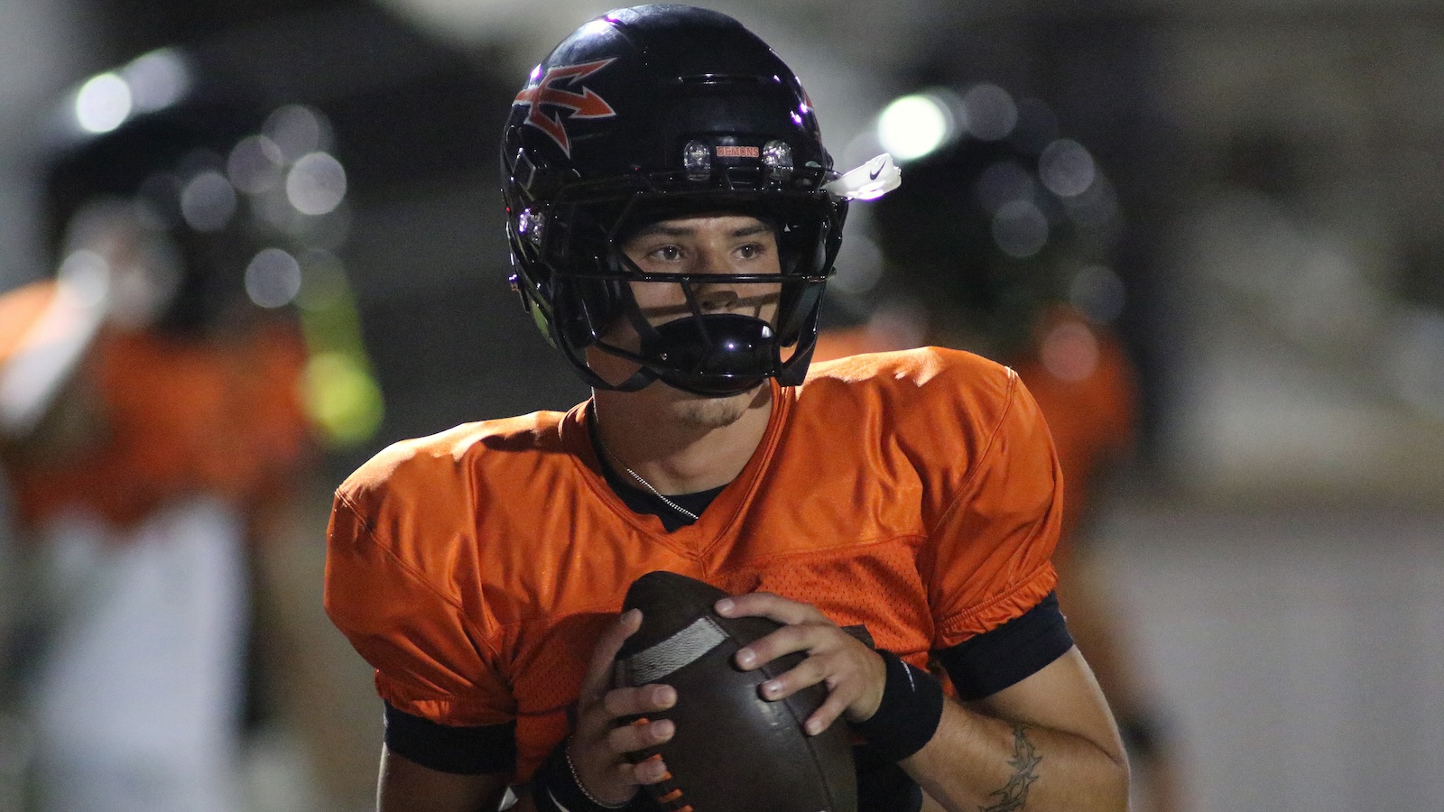American football player in an orange jersey and black helmet gripping a football.