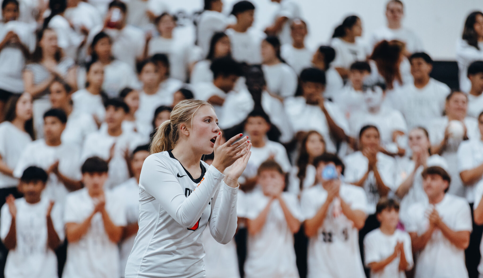 2C5A3453 | Press Pass Sports Female athlete in a white uniform clapping as a large crowd wearing white cheers in the stands behind her.