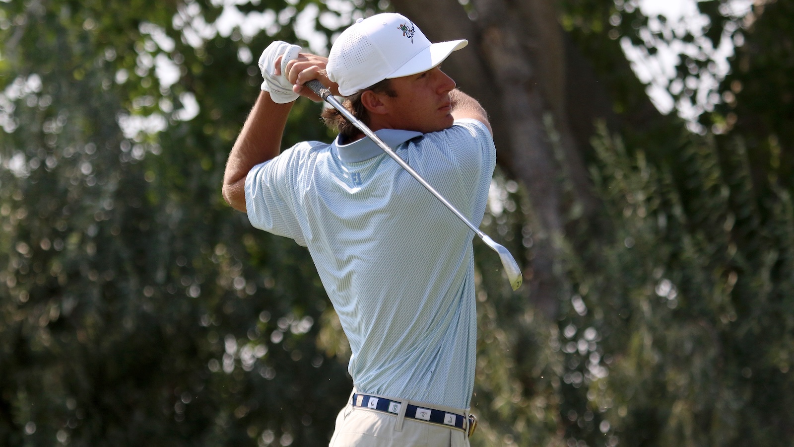 Male golfer in a light blue polo swinging a golf club on a sunny course. (informative)
